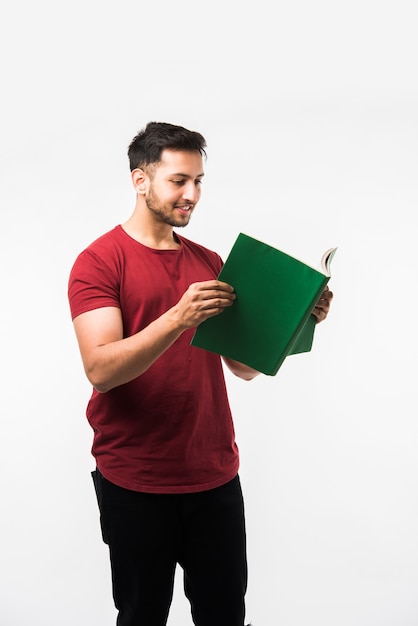 Estudiante universitario indio con libro, leyendo o mostrando la copa de la victoria, premio mientras está de pie aislado sobre fondo blanco.