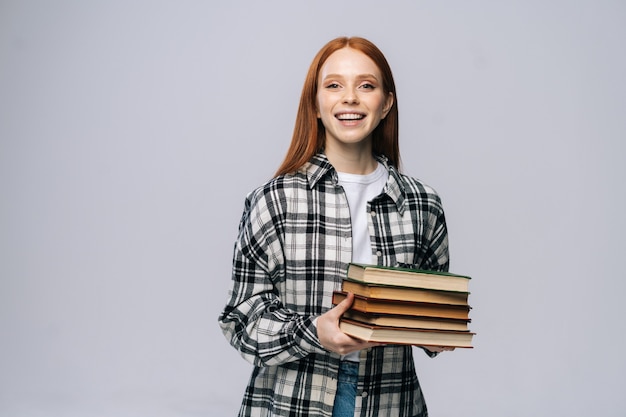 Estudiante universitario joven sonriente alegre que sostiene el libro y que mira la cámara