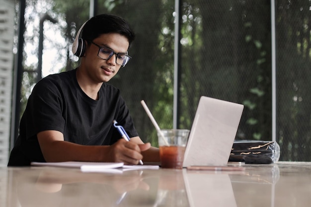 Estudiante universitario masculino asiático que estudia usando una computadora portátil en la cafetería o cafetería