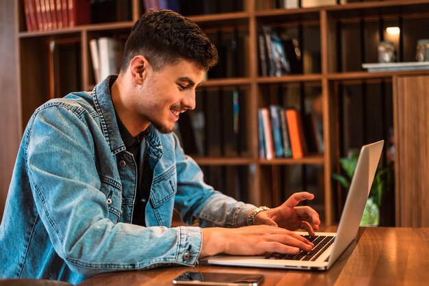 Un estudiante universitario masculino feliz que usa una computadora portátil en una biblioteca universitaria
