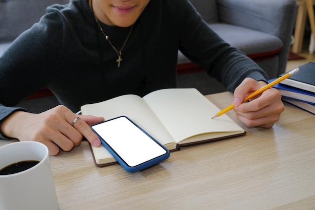 Estudiante universitario masculino joven que hace algunos deberes y que usa el teléfono inteligente.