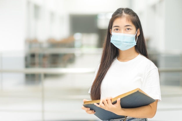 Estudiante universitario de mujer asiática en relajado casual regreso a la escuela con mascarilla médica en el campus