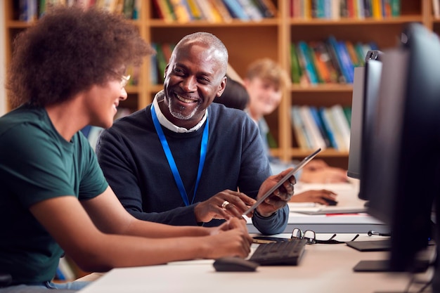 Estudiante universitario o universitario masculino que trabaja en la computadora en la biblioteca siendo ayudado por un tutor