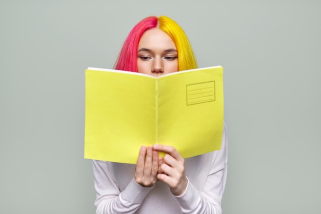 Estudiante universitario serio leyendo un cuaderno cerca de la cubierta amarilla lugar para el texto Chica adolescente sobre fondo de estudio claro