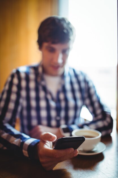 Estudiante usando un teléfono móvil mientras toma un café