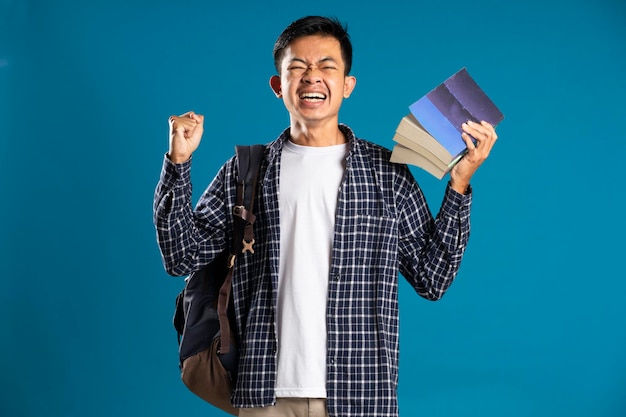 Estudiante varón con camisa emocionada levantando la mano celebrando el éxito aislado de fondo azul