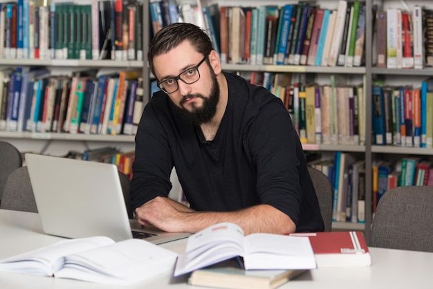 Estudiante varón feliz con portátil en la biblioteca