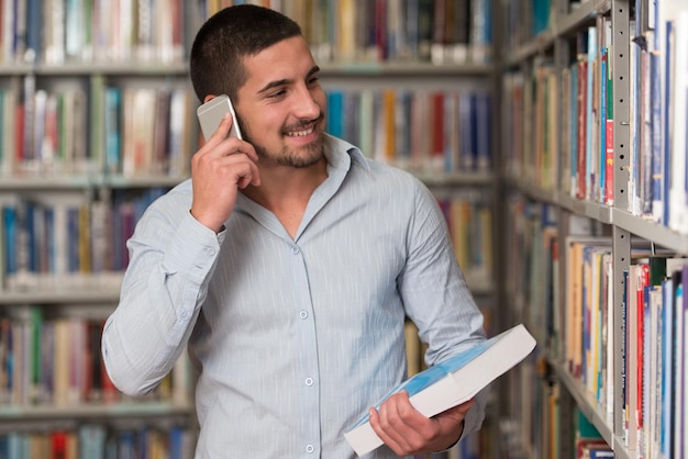 Estudiante varón hablando por teléfono en la biblioteca con poca profundidad de campo.