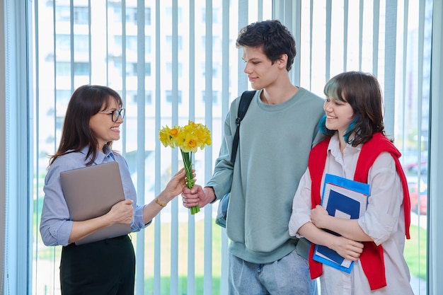 Foto estudiantes adolescentes felicitando a la maestra con un ramo de flores