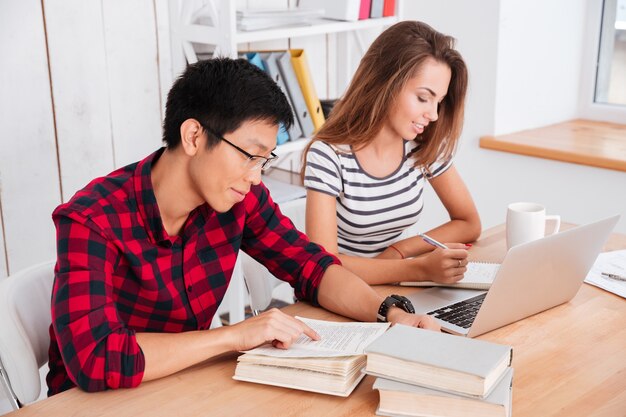 Estudiantes alegres que trabajan en el aula. Chica escribiendo y sentado cerca de la computadora portátil