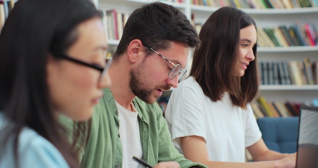 Los estudiantes amistosos se sientan en el escritorio en la escritura de la biblioteca discuten el proyecto colaborativo que se prepara para los exámenes de la escuela secundaria Concepto de estudio de educación universitaria