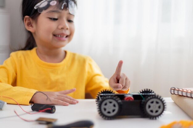 Los estudiantes asiáticos aprenden en casa en la codificación de coches robóticos y cables de placa electrónica en STEM STEAM matemáticas ingeniería ciencia tecnología código informático en robótica para niños concepto