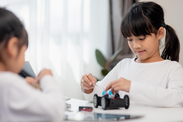 Los estudiantes asiáticos aprenden en casa en la codificación de coches robóticos y cables de placa electrónica en STEM STEAM matemáticas ingeniería ciencia tecnología código informático en robótica para niños concepto