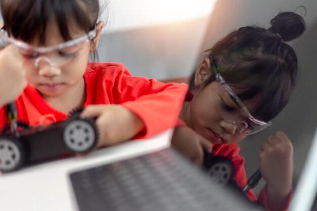 Los estudiantes asiáticos aprenden en casa en la codificación de coches robóticos y cables de placa electrónica en STEM STEAM matemáticas ingeniería ciencia tecnología código informático en robótica para niños concepto