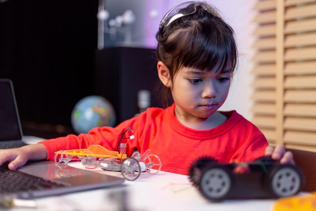 Los estudiantes asiáticos aprenden en casa en la codificación de coches robóticos y cables de placa electrónica en STEM STEAM matemáticas ingeniería ciencia tecnología código informático en robótica para niños concepto