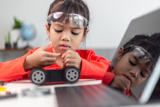 Los estudiantes asiáticos aprenden en casa en la codificación de coches robóticos y cables de placa electrónica en STEM STEAM matemáticas ingeniería ciencia tecnología código informático en robótica para niños concepto