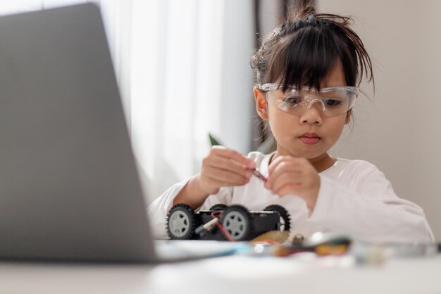 Los estudiantes asiáticos aprenden en casa en la codificación de coches robóticos y cables de placa electrónica en STEM STEAM matemáticas ingeniería ciencia tecnología código informático en robótica para niños concepto