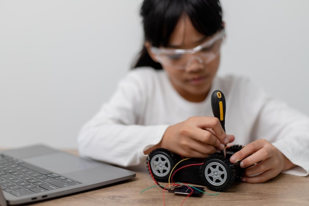 Los estudiantes asiáticos aprenden en casa en la codificación de coches robóticos y cables de placa electrónica en STEM STEAM matemáticas ingeniería ciencia tecnología código informático en robótica para niños concepto