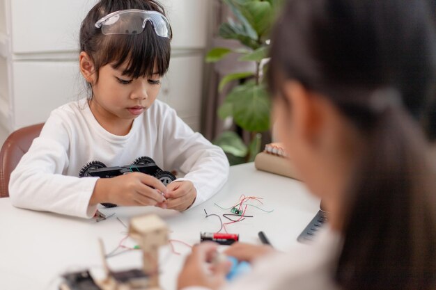Los estudiantes asiáticos aprenden en casa en la codificación de coches robóticos y cables de placa electrónica en STEM STEAM matemáticas ingeniería ciencia tecnología código informático en robótica para niños concepto