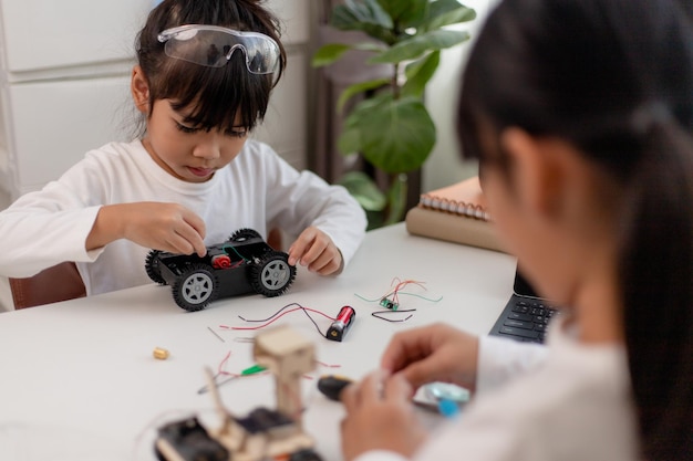 Los estudiantes asiáticos aprenden en casa en la codificación de coches robóticos y cables de placa electrónica en STEM STEAM matemáticas ingeniería ciencia tecnología código informático en robótica para niños concepto