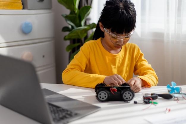 Los estudiantes asiáticos aprenden en casa en la codificación de coches robóticos y cables de placa electrónica en STEM STEAM matemáticas ingeniería ciencia tecnología código informático en robótica para niños concepto