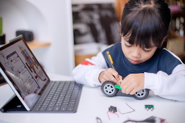 Los estudiantes asiáticos aprenden en casa en la codificación de coches robóticos y cables de placa electrónica en STEM STEAM matemáticas ingeniería ciencia tecnología código informático en robótica para niños concepto
