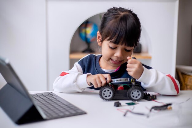 Los estudiantes asiáticos aprenden en casa en la codificación de coches robóticos y cables de placa electrónica en STEM STEAM matemáticas ingeniería ciencia tecnología código informático en robótica para niños concepto