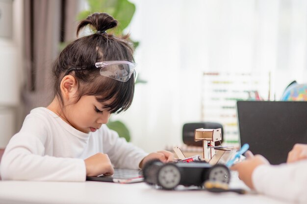 Los estudiantes asiáticos aprenden en casa en la codificación de coches robóticos y cables de placa electrónica en STEM STEAM matemáticas ingeniería ciencia tecnología código informático en robótica para niños concepto