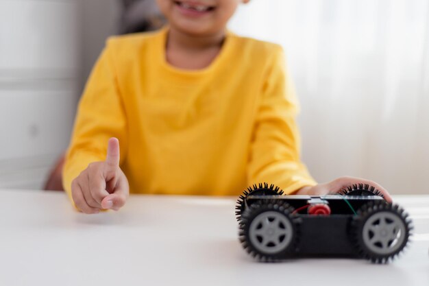 Los estudiantes asiáticos aprenden en casa en la codificación de coches robóticos y cables de placa electrónica en STEM STEAM matemáticas ingeniería ciencia tecnología código informático en robótica para niños concepto