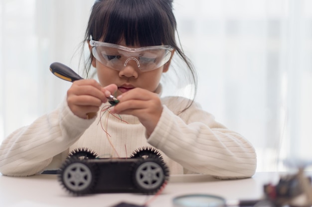 Los estudiantes asiáticos aprenden en casa codificando autos robot y cables de placas electrónicas en STEM STEAM matemáticas ingeniería ciencia tecnología código informático en robótica para niños concepto