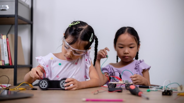 Los estudiantes asiáticos aprenden en casa codificando coches robot y cables de placas electrónicas en STEM STEAM matemáticas ingeniería ciencia tecnología código informático en robótica para conceptos infantiles