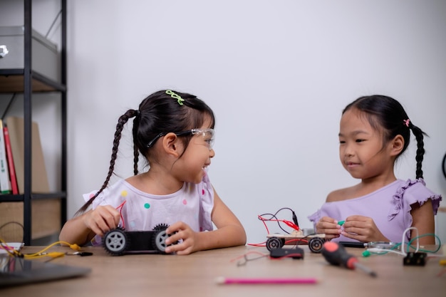 Los estudiantes asiáticos aprenden en casa codificando coches robot y cables de placas electrónicas en STEM STEAM matemáticas ingeniería ciencia tecnología código informático en robótica para conceptos infantiles