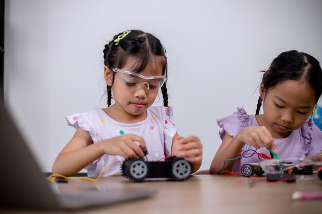 Los estudiantes asiáticos aprenden en casa codificando coches robot y cables de placas electrónicas en STEM STEAM matemáticas ingeniería ciencia tecnología código informático en robótica para conceptos infantiles