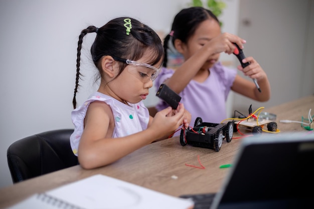 Los estudiantes asiáticos aprenden en casa codificando coches robot y cables de placas electrónicas en STEM STEAM matemáticas ingeniería ciencia tecnología código informático en robótica para conceptos infantiles