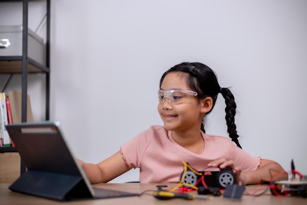 Los estudiantes asiáticos aprenden en casa codificando coches robot y cables de placas electrónicas en STEM STEAM matemáticas ingeniería ciencia tecnología código informático en robótica para conceptos infantiles