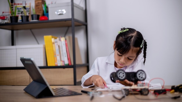 Los estudiantes asiáticos aprenden en casa codificando coches robot y cables de placas electrónicas en STEM STEAM matemáticas ingeniería ciencia tecnología código informático en robótica para conceptos infantiles