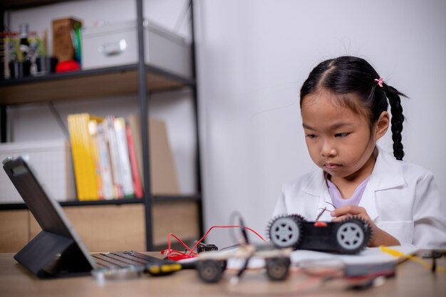 Los estudiantes asiáticos aprenden en casa codificando coches robot y cables de placas electrónicas en STEM STEAM matemáticas ingeniería ciencia tecnología código informático en robótica para conceptos infantiles