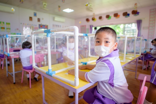 Estudiantes asiáticos en aulas de jardín de infantes en escuelas de Tailandia usan máscaras y distanciamiento social en las aulas