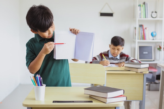 Estudiantes asiáticos que estudian en clase y presentan la página de su libro en blanco para maqueta