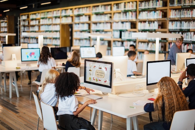 Estudiantes en la biblioteca usando computadoras Diverso grupo de niños aprendiendo entorno de biblioteca con computadoras Niños involucrados en actividades educativas Jóvenes estudiantes aprendiendo en computadoras en la biblioteca escolar