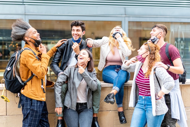 Estudiantes de diferentes etnias bromeando y riendo juntos durante el período epidémico jóvenes irresponsables que usan la máscara facial incorrectamente nuevo concepto normal sin distanciamiento social