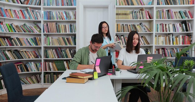 Los estudiantes discuten sobre el uso de la computadora portátil y se preparan para los exámenes juntos, ayudando a investigar temas para la asignación en papel Biblioteca universitaria