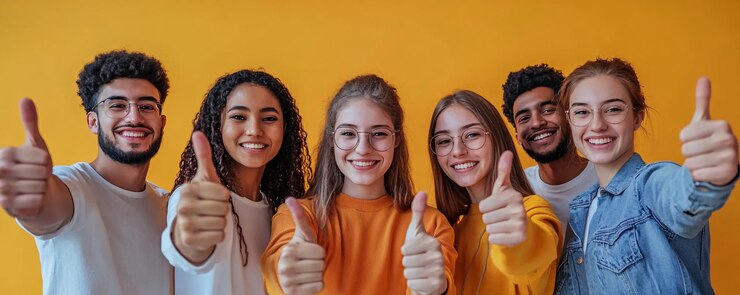 Estudiantes diversos felices mostrando los pulgares hacia arriba celebrando el éxito sobre un fondo amarillo
