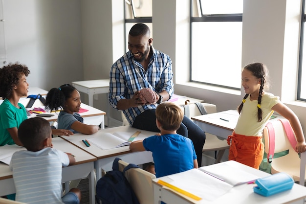 Estudiantes elementales multirraciales felices mirando a un joven maestro masculino multirracial que muestra un modelo cerebral