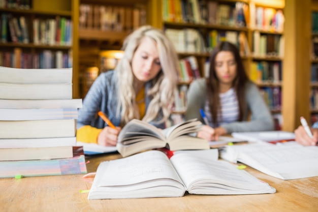 Estudiantes escribiendo notas con pila de libros en el mostrador de la biblioteca