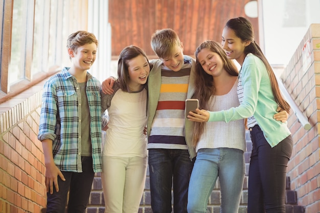 Foto estudiantes de la escuela sonriente de pie en la escalera con teléfono móvil