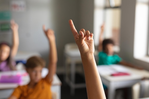 Estudiantes de escuelas primarias multirraciales con las manos levantadas durante la clase en el aula. sin alteración, educación, aprendizaje, inteligencia, infancia, estudio y concepto escolar.