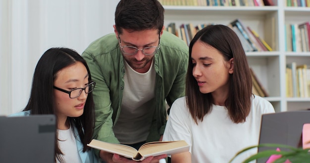 Los estudiantes estudian en equipo juntos usando una computadora portátil y se preparan para el examen en la biblioteca. Los jóvenes multiétnicos hablan en grupo mirando la computadora.