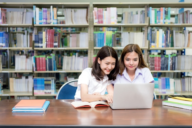 Estudiantes felices asiáticos con ordenador portátil trabajando y estudiando en la biblioteca.