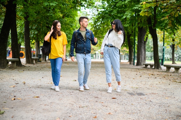 Estudiantes felices caminando al aire libre y hablando entre sí, de cuerpo entero